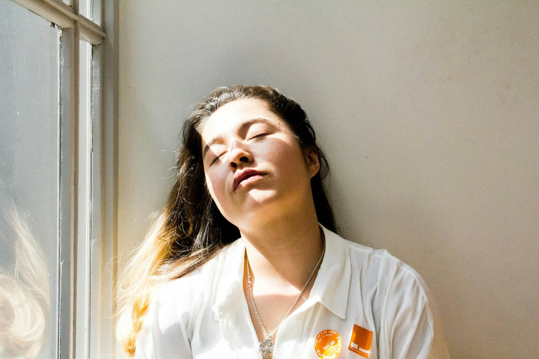 A woman resting in morning light by a window with her eyes closed