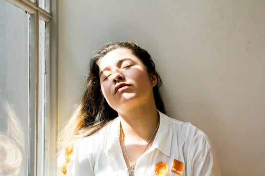 A woman resting in morning light by a window with her eyes closed