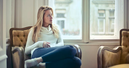 A woman sitting in an armchair by a bright window, thinking