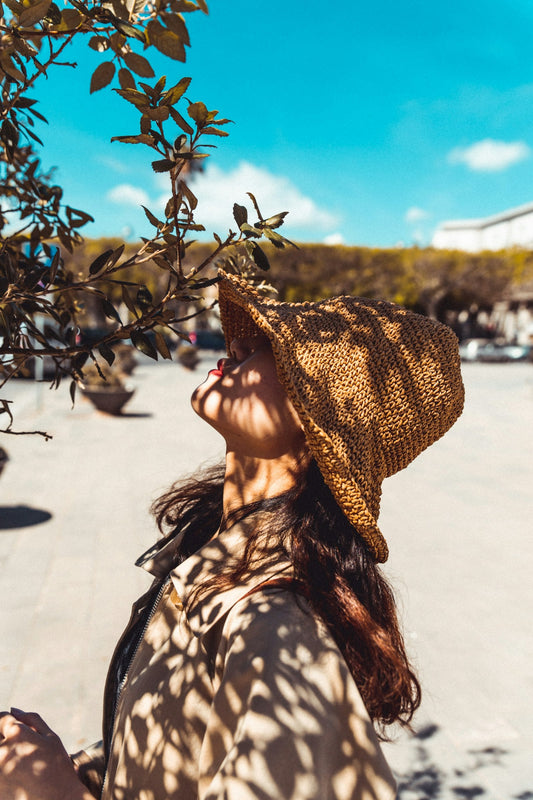 Woman in a straw sun hat standing in the shade of a tree