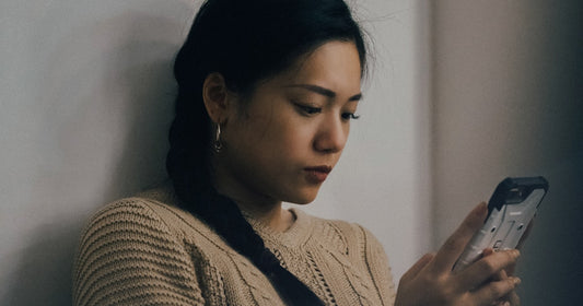 A woman in a cream knitted jumper reading something on her phone, thoughtful, soft indoor light