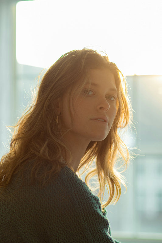 A woman with long auburn hair in a green jumper, sitting in warm window light