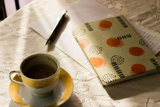 A notebook, a pen and a cup on a lace tablecloth in warm morning sunlight