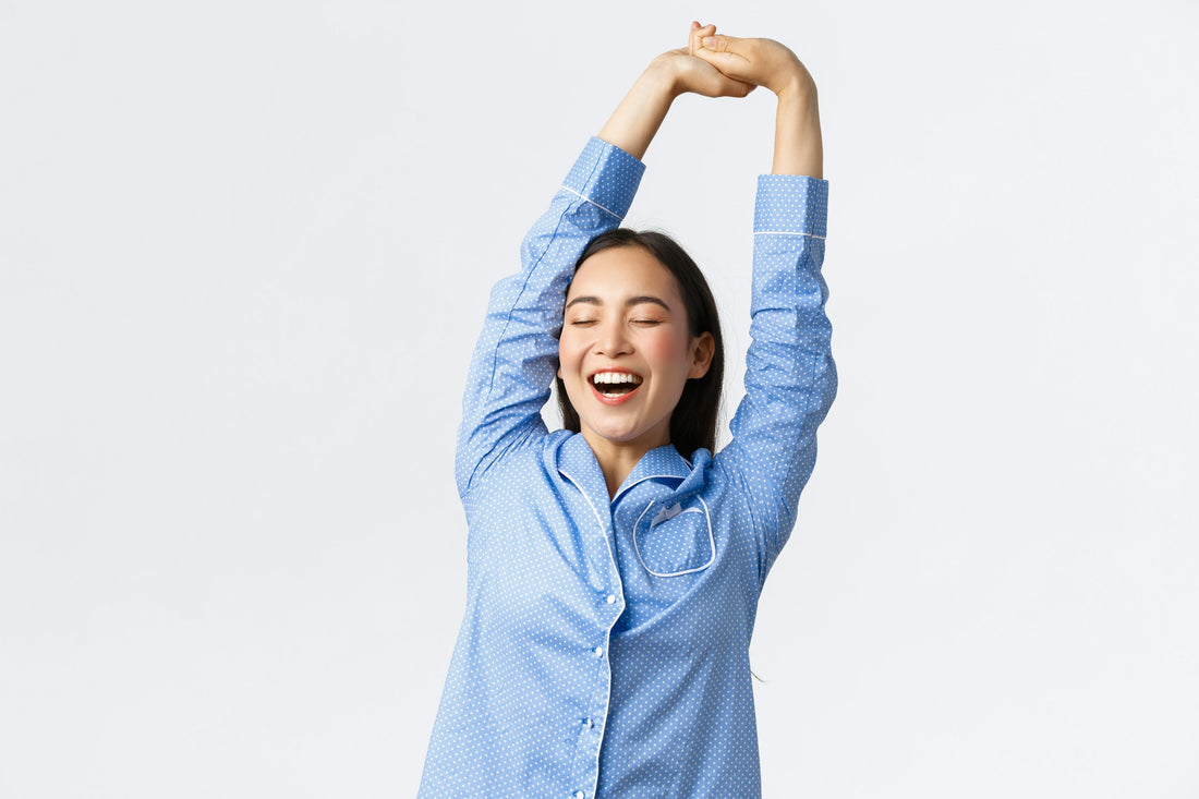 Woman in blue pyjamas stretching and laughing, waking refreshed