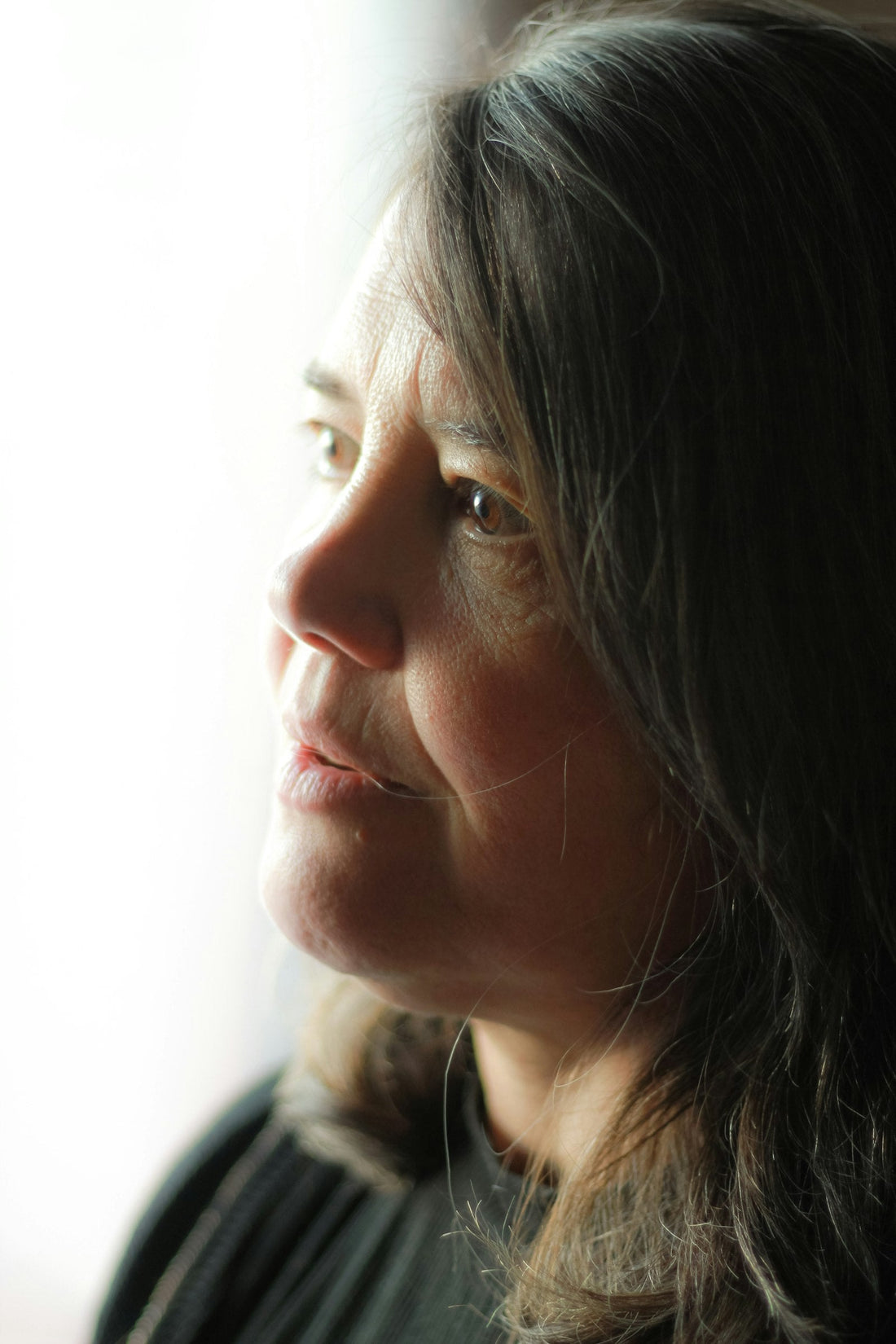 Woman looking out of a window, thoughtful, in natural light