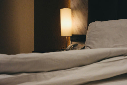 Bedside lamp lit beside a made bed at night