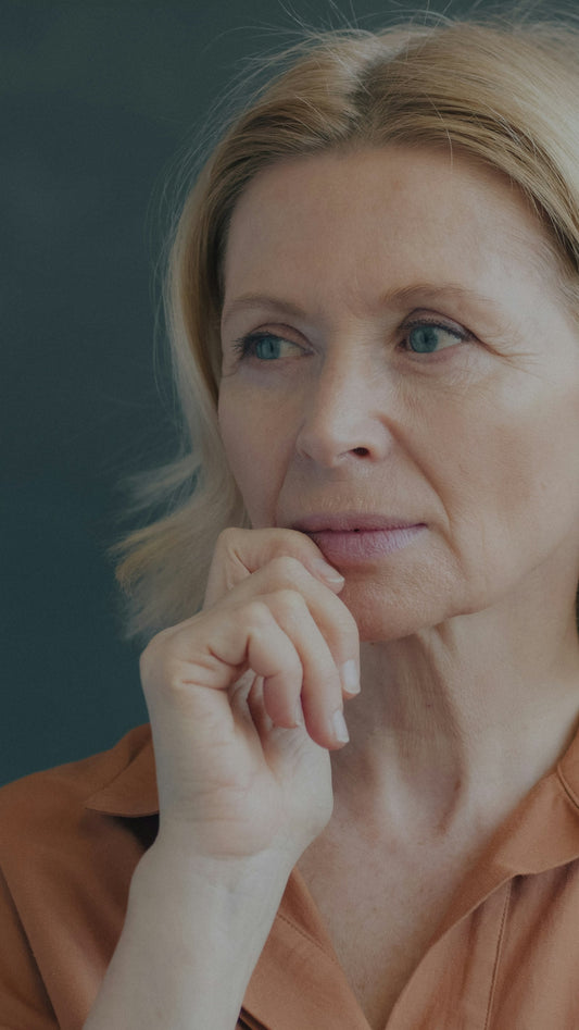 A woman in her 50s with blonde hair, resting her chin on her hand and looking thoughtful